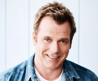 Man smiling, wearing a denim shirt, against a light background.