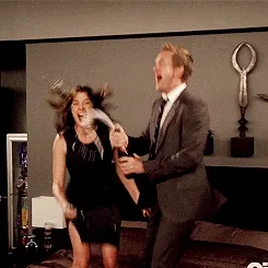 Two people in a hotel room celebrating by spraying champagne, both looking excited and joyful.