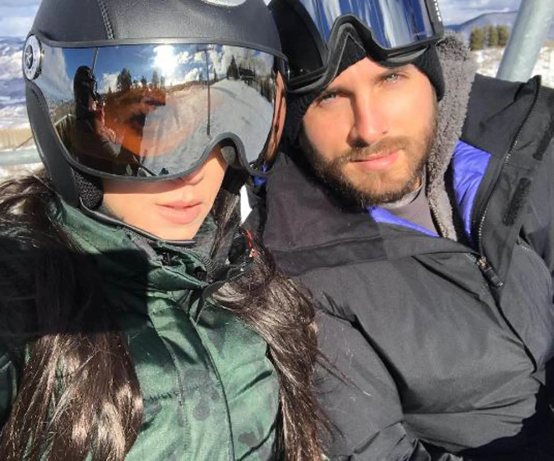 Two people in ski gear taking a selfie on a snowy mountain, one wearing reflective goggles.