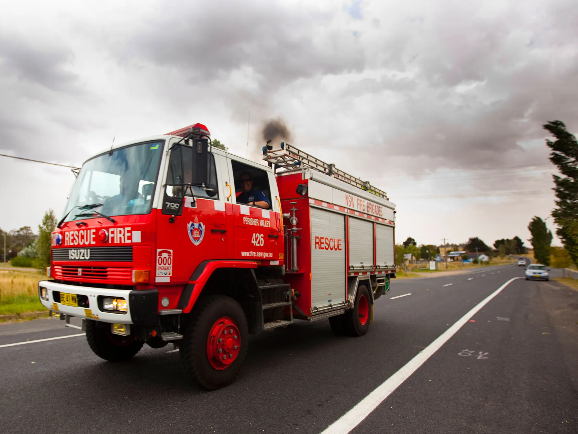 Fire truck from NSW Fire Brigades driving on a highway under a cloudy sky.