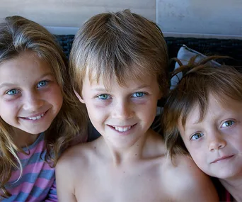 Three smiling children with blue eyes, close together, looking at the camera.