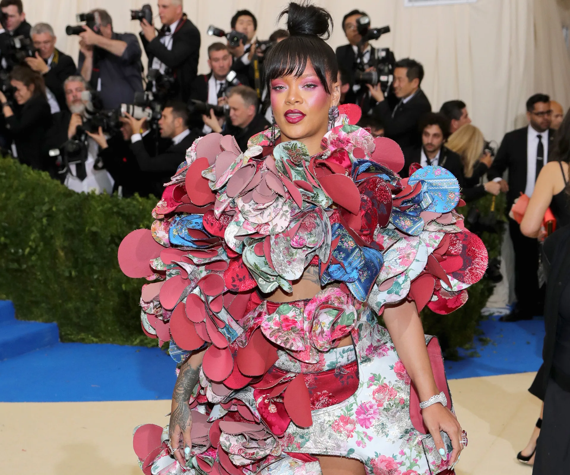 A person in a vibrant, multicolored floral outfit on the red carpet, surrounded by photographers.