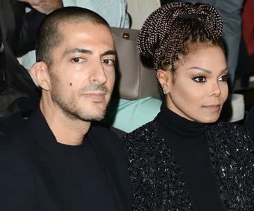 A couple seated together, dressed in black, looking serious and contemplative.