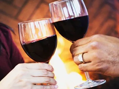 couple holding up glass of red wine 