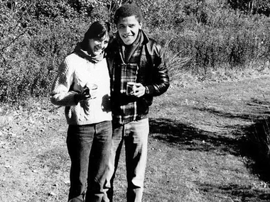 A young couple stands outdoors holding cups, smiling for the camera in a black and white photo.