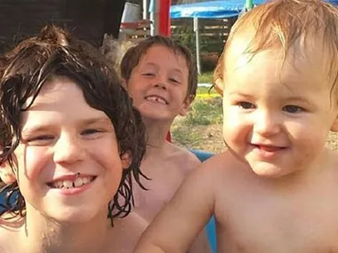 Three young children smiling and playing outdoors in a backyard setting.
