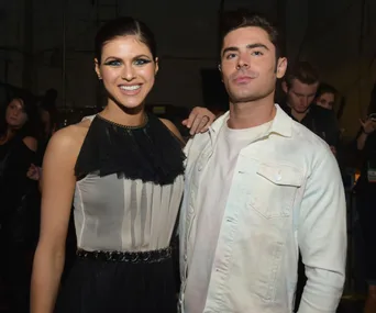Two people smiling at an event, one wearing a black and white dress, the other in a white jacket.