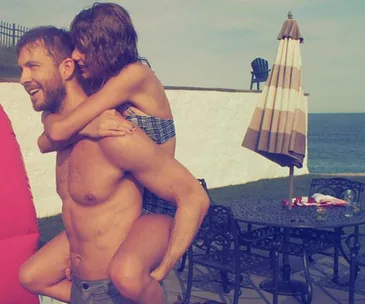 A man giving a piggyback ride to a woman by a poolside with ocean view in the background.