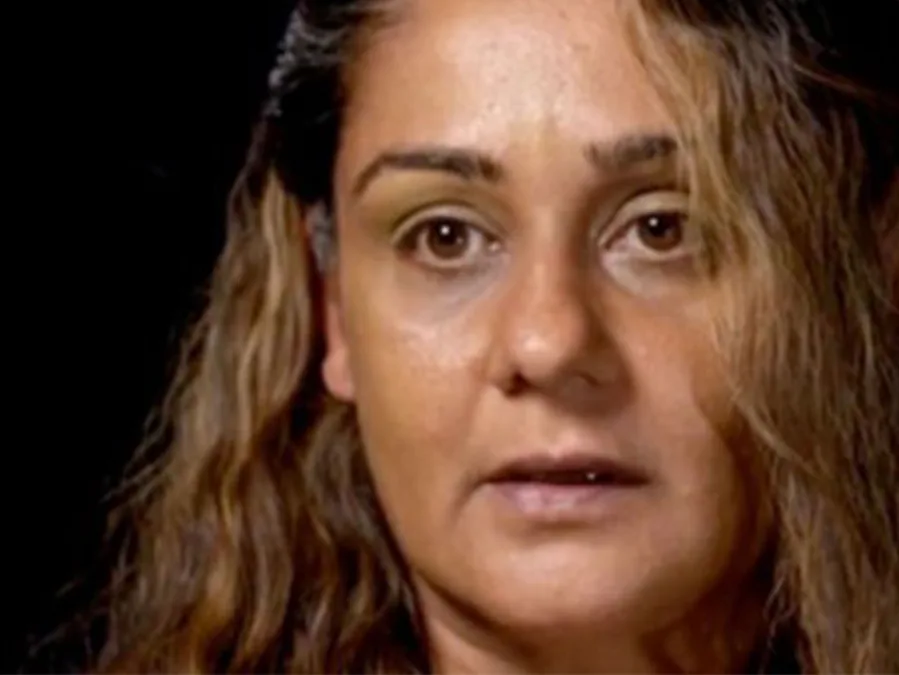 A woman with long brown hair and a serious expression against a dark background.