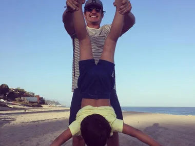 Father and son playing on the beach, dad holding son upside down, both smiling.