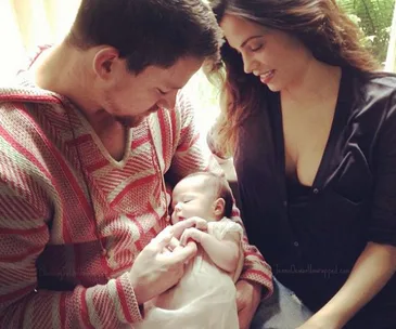A couple lovingly gazes at their newborn baby, who is peacefully sleeping in the father's arms.