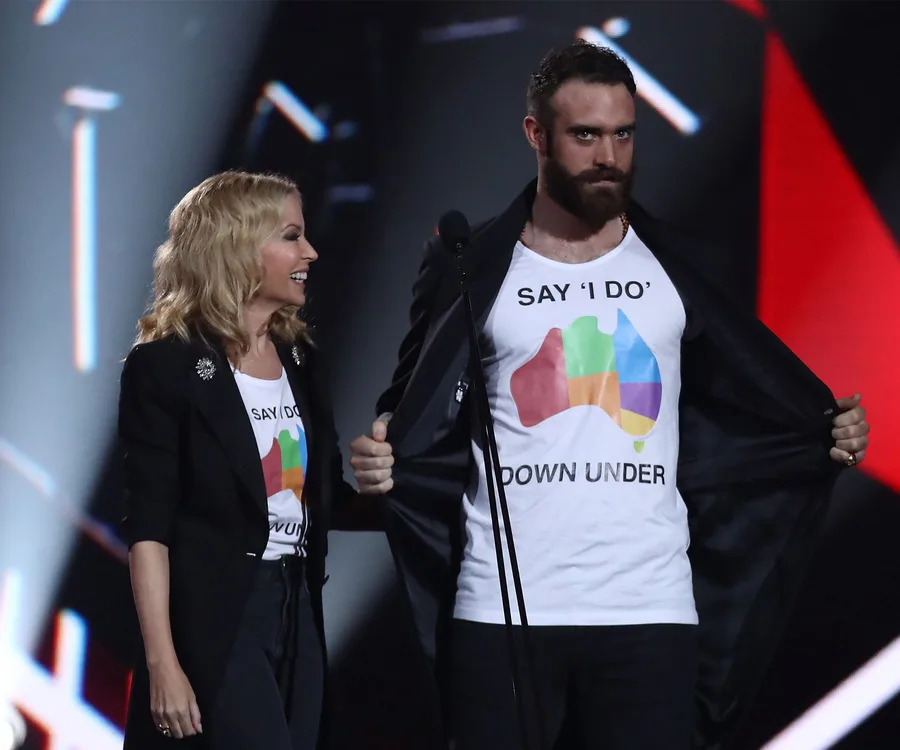 Two people on stage wearing "Say 'I Do' Down Under" t-shirts with a colorful map of Australia design.