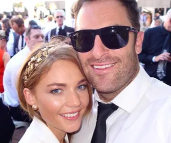 A couple smiling at an outdoor event, surrounded by people in formal attire.