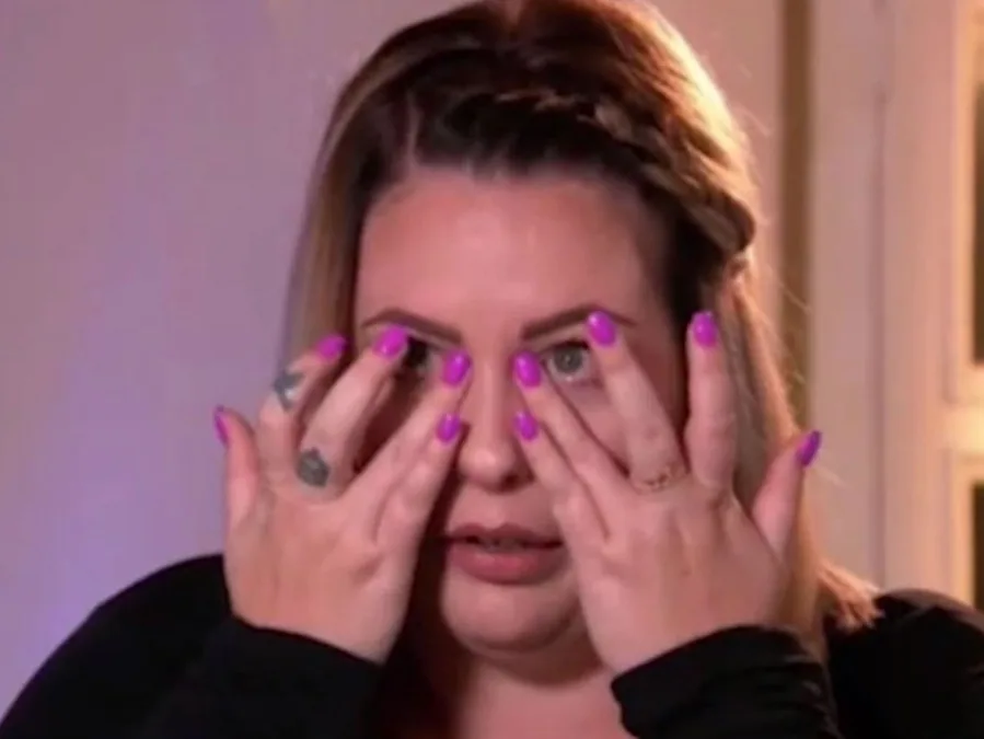 A woman with pink nails covers her face with her hands.