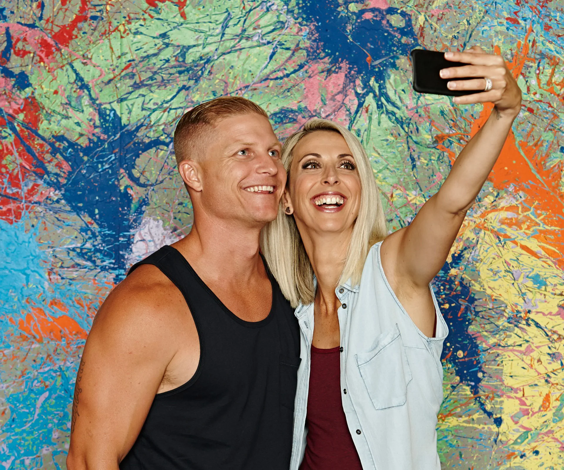 A couple taking a selfie in front of a colorful, abstract graffiti wall, smiling and joyful.
