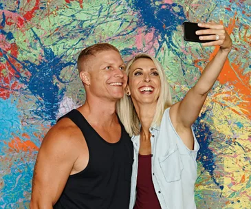 A couple taking a selfie in front of a colorful, abstract graffiti wall, smiling and joyful.