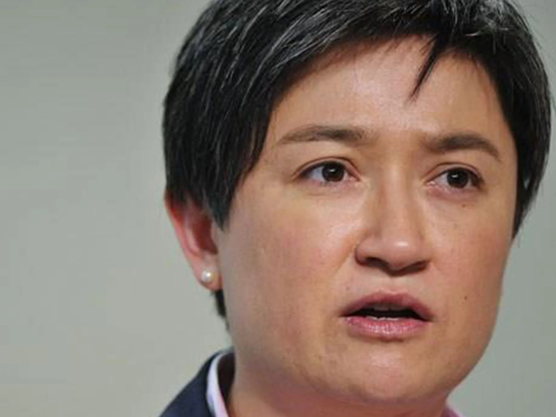 A person with short dark hair is speaking, looking serious, with a neutral background.