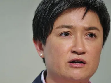 A person with short dark hair is speaking, looking serious, with a neutral background.