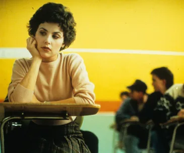 Audrey Horne in a classroom, resting her chin on her hand, looking thoughtful in "Twin Peaks."