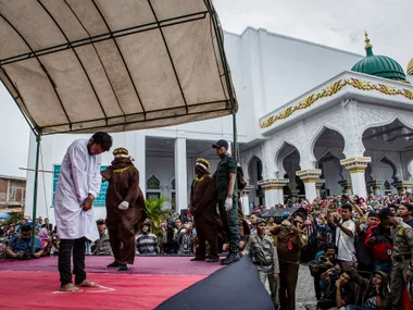 Public caning in Indonesia, with officials and a crowd watching outside a mosque.