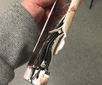 A damaged iPhone with a cracked screen, partially open and showing internal components, held in a hand.