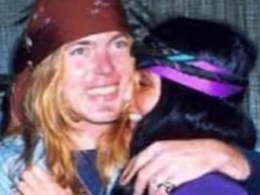 Two people with long hair and headbands embrace, smiling closely together.