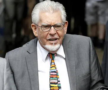 A man in a gray suit and colorful tie, outdoors in a crowd.