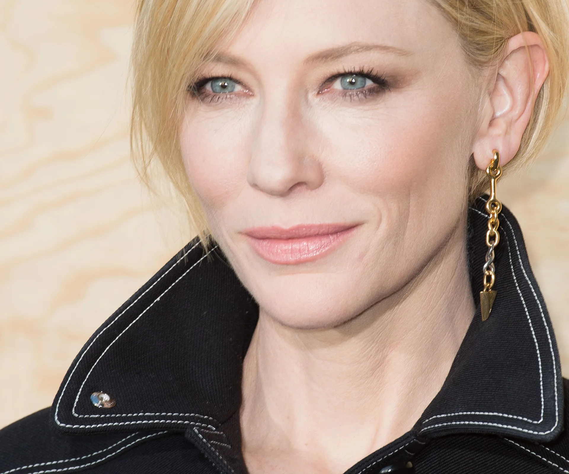 A close-up of a person with blonde hair, wearing a dark jacket and gold earring, looking slightly to the right.