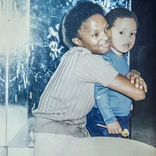 A woman hugging a young child, holding a lollipop, with a mirror reflecting light in the background.