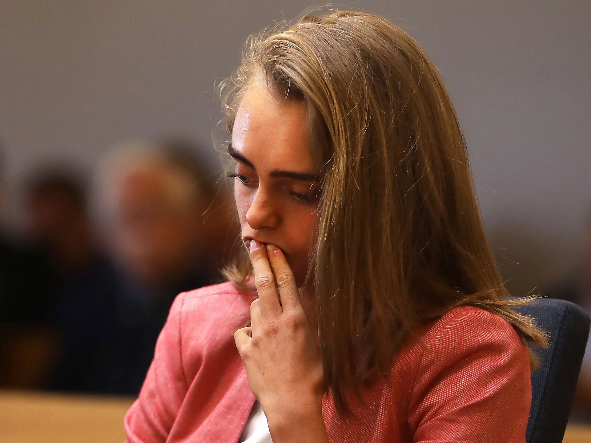 A person in court, appearing pensive, with hand on face, wearing a pink blazer.