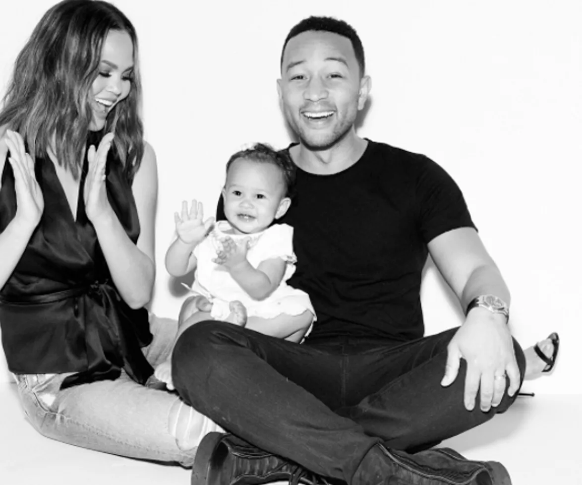 Family sitting together, smiling and clapping, with a happy toddler in the middle. Black and white photo.