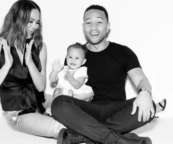 Family sitting together, smiling and clapping, with a happy toddler in the middle. Black and white photo.