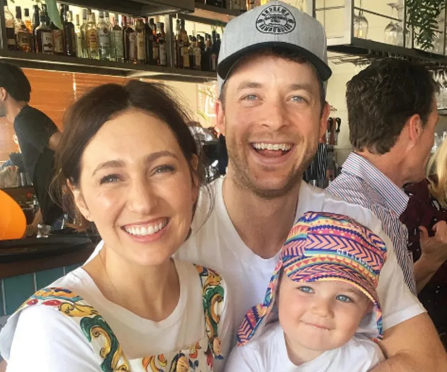 Smiling family at a bar, woman in patterned dress, man in cap, child in colorful hat.