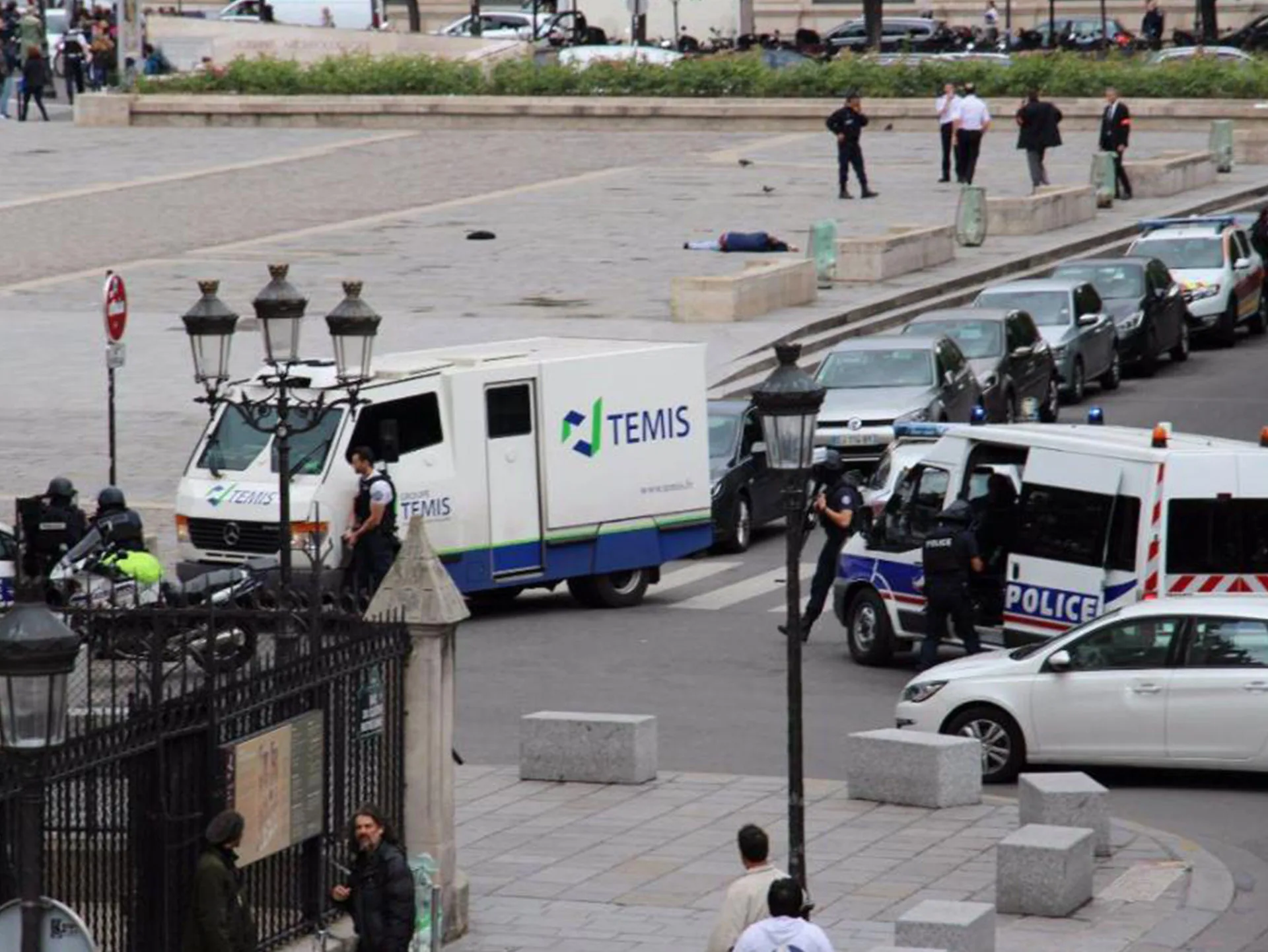 Police vehicles and officers respond to an incident near Notre-Dame Cathedral, with a person lying on the ground.
