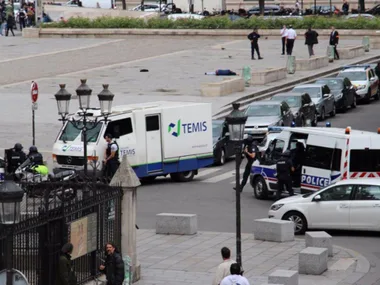Police vehicles and officers respond to an incident near Notre-Dame Cathedral, with a person lying on the ground.
