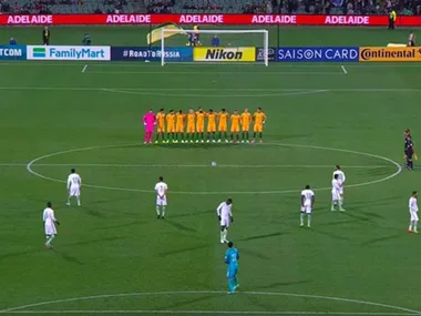 Soccer teams on field, one in yellow, one in white, during pre-match event in Adelaide stadium.