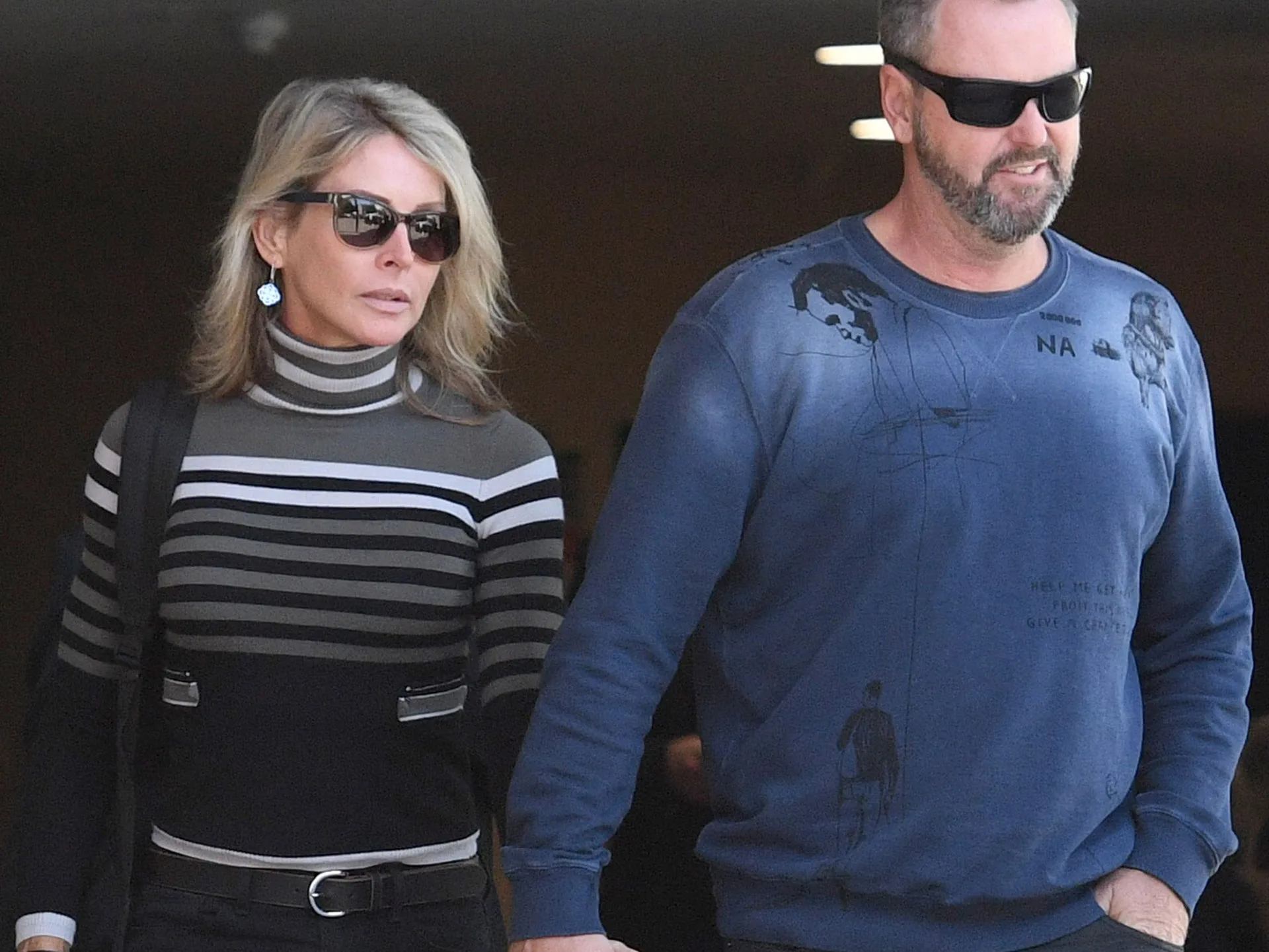 A man and woman in sunglasses walking together, dressed in casual attire.