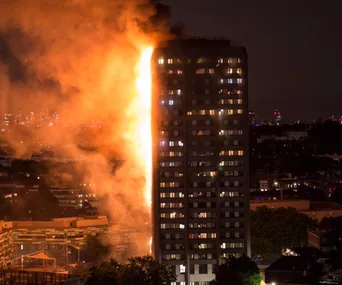 A high-rise building engulfed in flames at night with smoke and fire on the exterior.