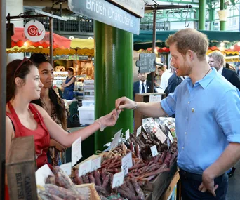 Prince Harry interacts with stall vendors at Borough Market, surrounded by charcuterie products.