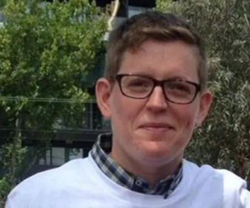A person outdoors wearing glasses and a white shirt, with trees in the background.