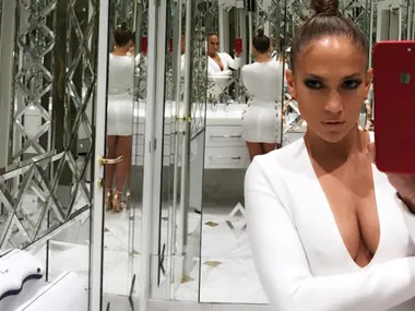 Woman in a white dress takes a mirror selfie in a luxurious, mirrored bathroom.
