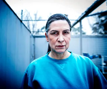Pamela Rabe as Joan Ferguson in "Wentworth," wearing a blue prison uniform with a serious expression.