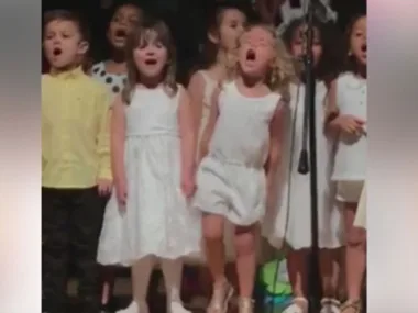 Children passionately sing on stage, with a blonde girl energetically performing in the center.