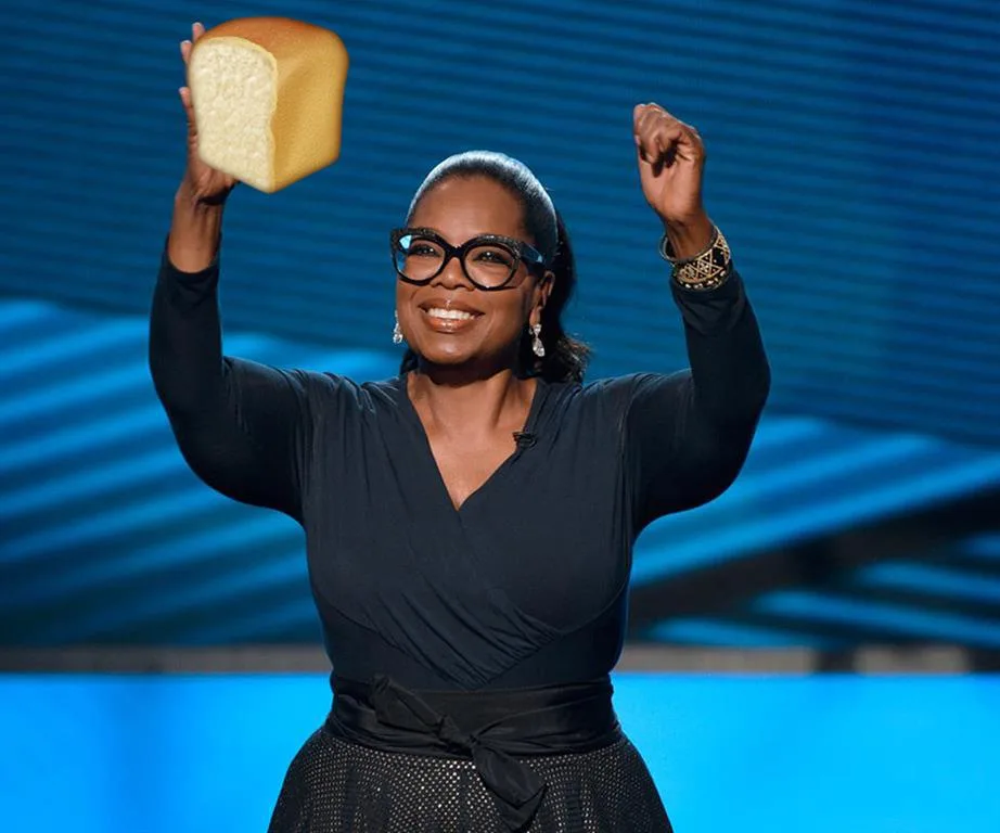 A person holding a loaf of bread triumphantly on a stage with a blue background.