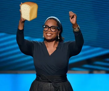 A person holding a loaf of bread triumphantly on a stage with a blue background.