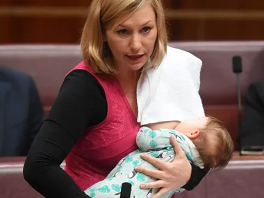 A woman breastfeeding her baby in a public setting, both wearing casual attire.