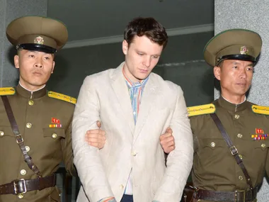 A person escorted by two uniformed guards inside a building.