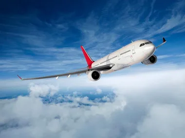 Commercial airplane flying above the clouds with a blue sky backdrop.