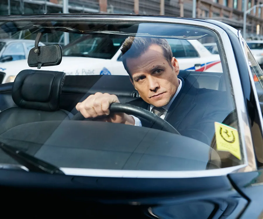 A suited man driving a car, focused and serious, from "Suits" Season 7 teaser.