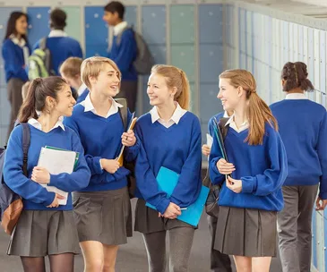 A group of four high school students in blue uniforms walk and talk in a hallway with lockers.